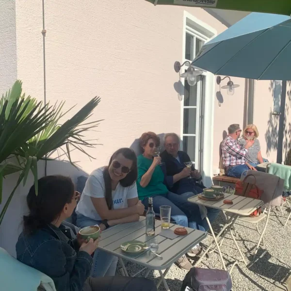 Kunden sitzen draußen, lachen beherzt und genießen edle Cocktails, Kaffee und Kaltgetränke